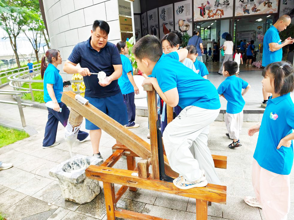 8 月15日，桃源街道总工会 “E 路安 - 南工守护”亲子非遗研学活动在光明区小隐非遗基地开展，辖区40 组新业态和户外劳动者家庭参与，在国学礼仪、传统手作与趣味团建中增进亲子情谊，沉浸式感受非遗魅力。亲子共同捶捣糯米，体验传统民俗乐趣。受访单位供图.jpg